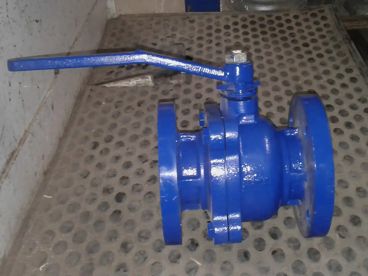 Flanged industrial ball valve with a blue painted two-piece body and a quarter-turn lever handle, mounted on a steel grating floor