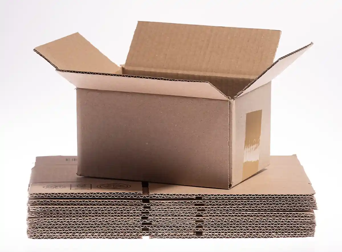 An assembled open corrugated cardboard carton box (Regular Slotted Container) resting on a stack of flat-folded corrugated boxes showing the fluted board edges