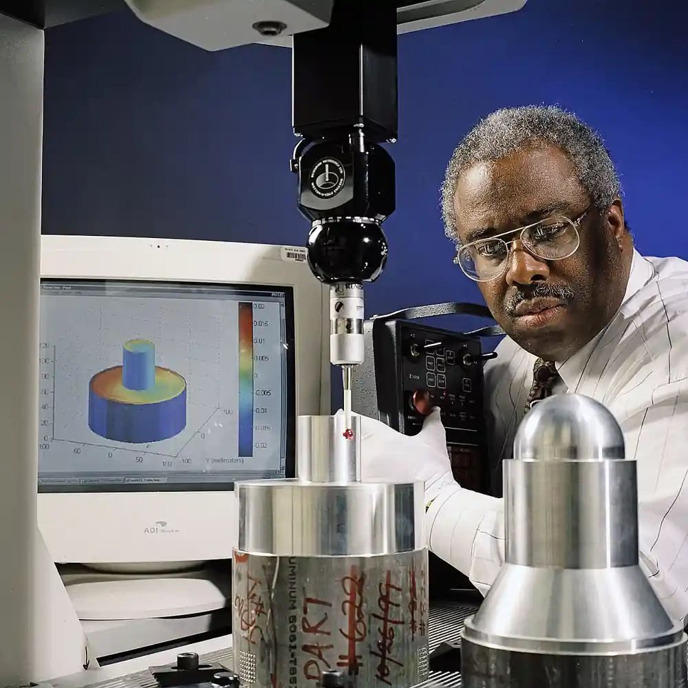 Coordinate measuring machine with ruby-tipped touch probe measuring a cylindrical metal part, with metrology software displayed on screen