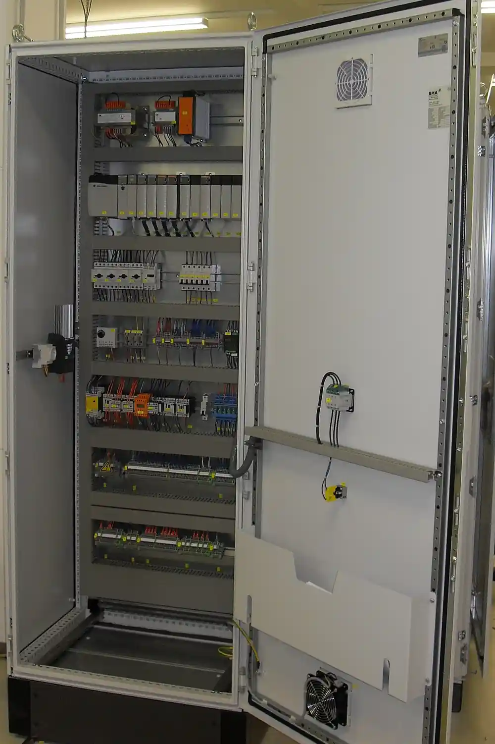 Open floor-standing industrial control cabinet with Allen-Bradley PLC, circuit breakers and terminal blocks on DIN rails