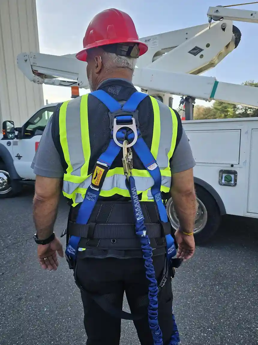 Rear view of a worker wearing a full body fall arrest harness, showing the dorsal D-ring centered between the shoulder blades with an energy-absorbing lanyard attached