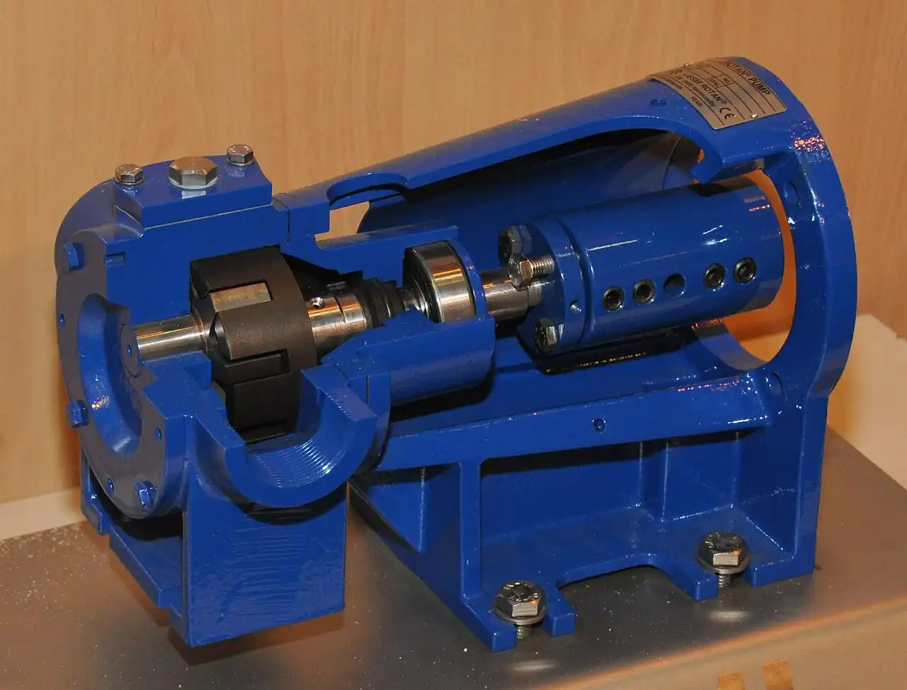 Cut-away of an industrial internal gear pump on its baseplate, with the blue cast-iron casing sectioned to expose the rotor, idler gear, drive shaft, and bearing