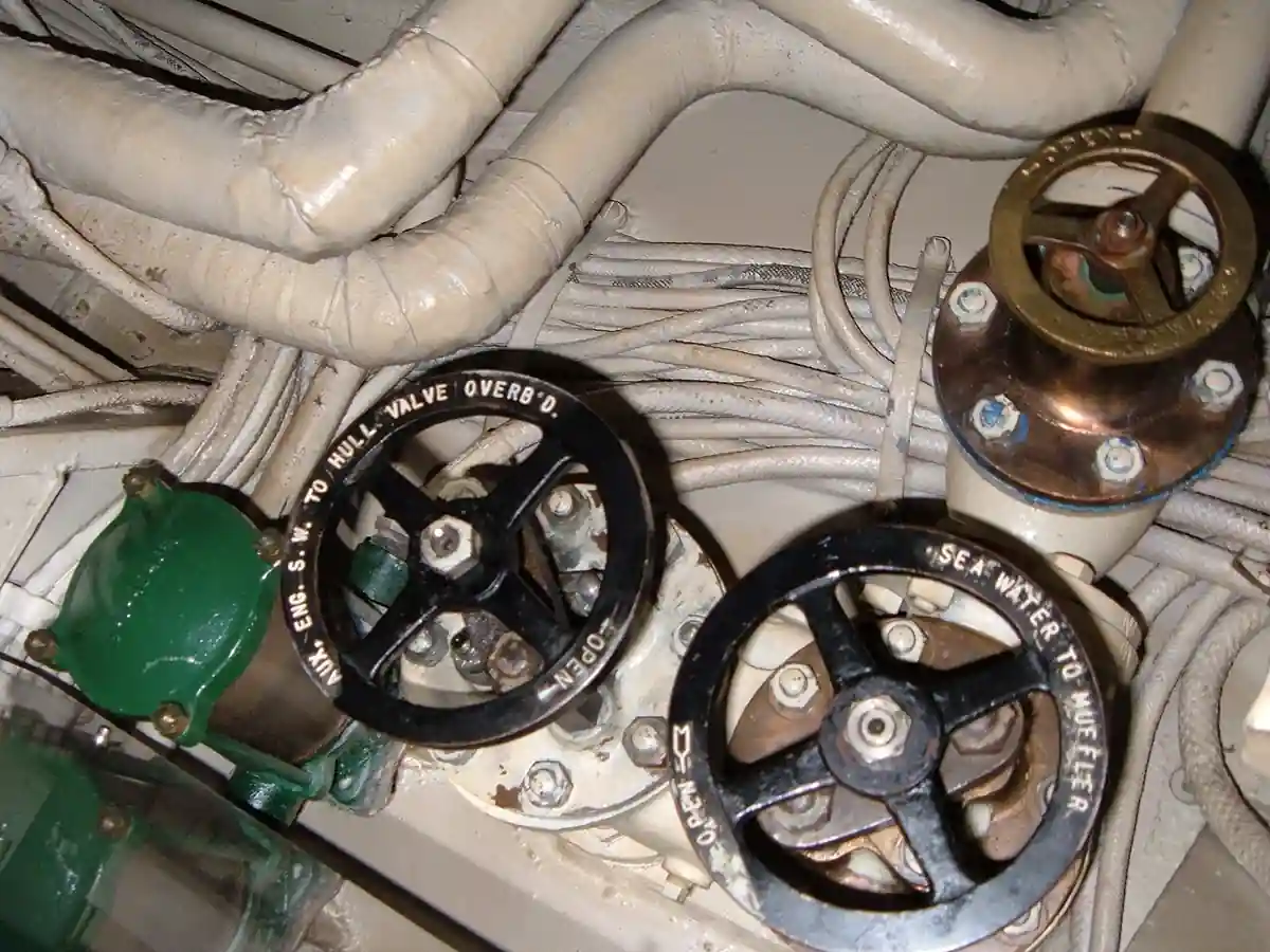 Shipboard sea water valves with labelled handwheels and a bronze-bonneted valve in the after engine room of submarine USS Pampanito