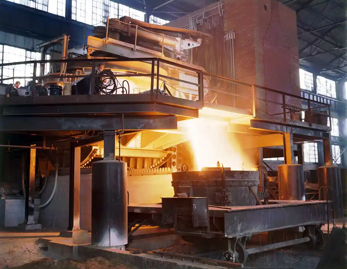 White-hot molten steel pouring from an electric melting furnace with electrode platform and furnace shell at a steel plant