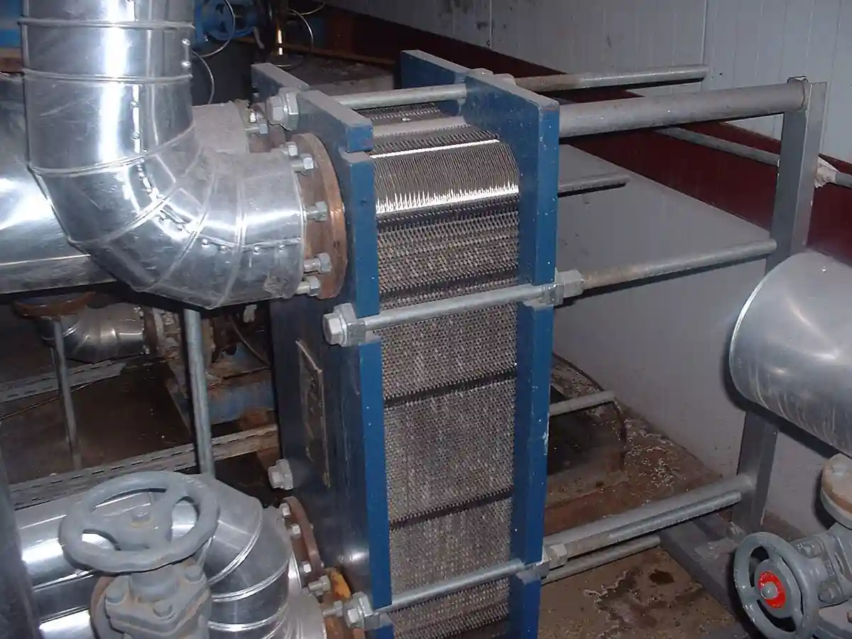 Gasketed plate-and-frame heat exchanger installed in a plant room, showing plate pack, blue frame and tie bolts