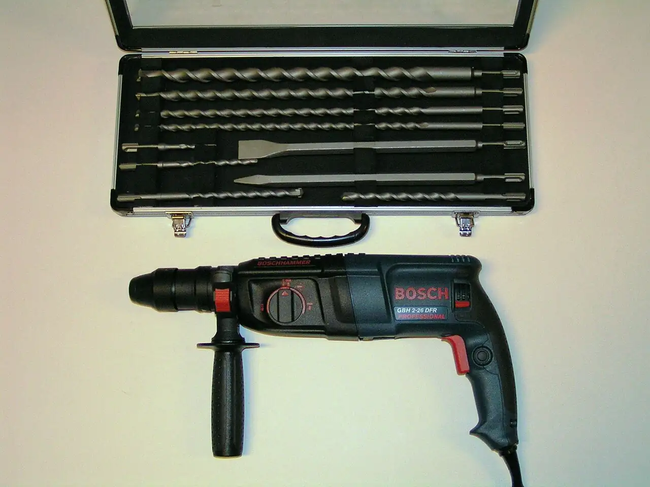 Bosch GBH 2-26 DFR Professional SDS-plus rotary hammer with mode-selector dial and side handle, beside a case of SDS-plus masonry drill bits and chisels