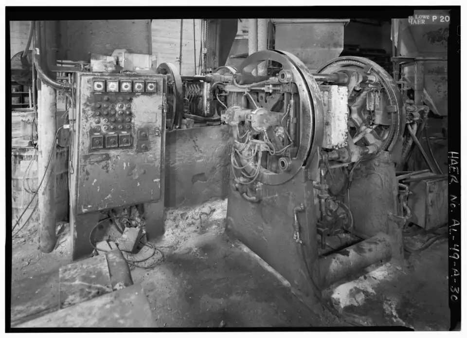 National shell core machine in a grey iron foundry: a round heated core box with sand blow heads and pneumatic clamps, a push-button control panel at left, and sand magazine hoppers above