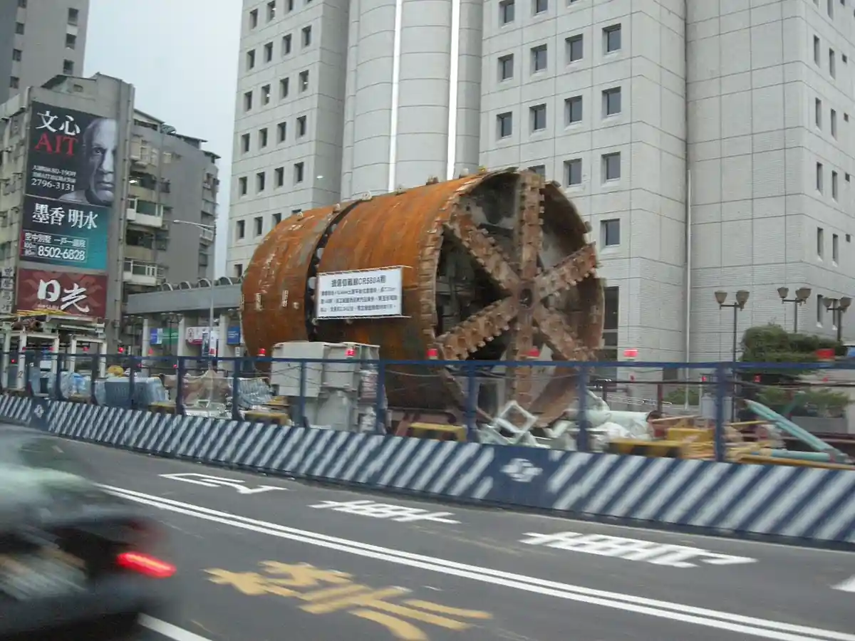 A cylindrical steel shield tunnel boring machine with its spoked cutterhead exposed at a Taipei MRT metro construction site