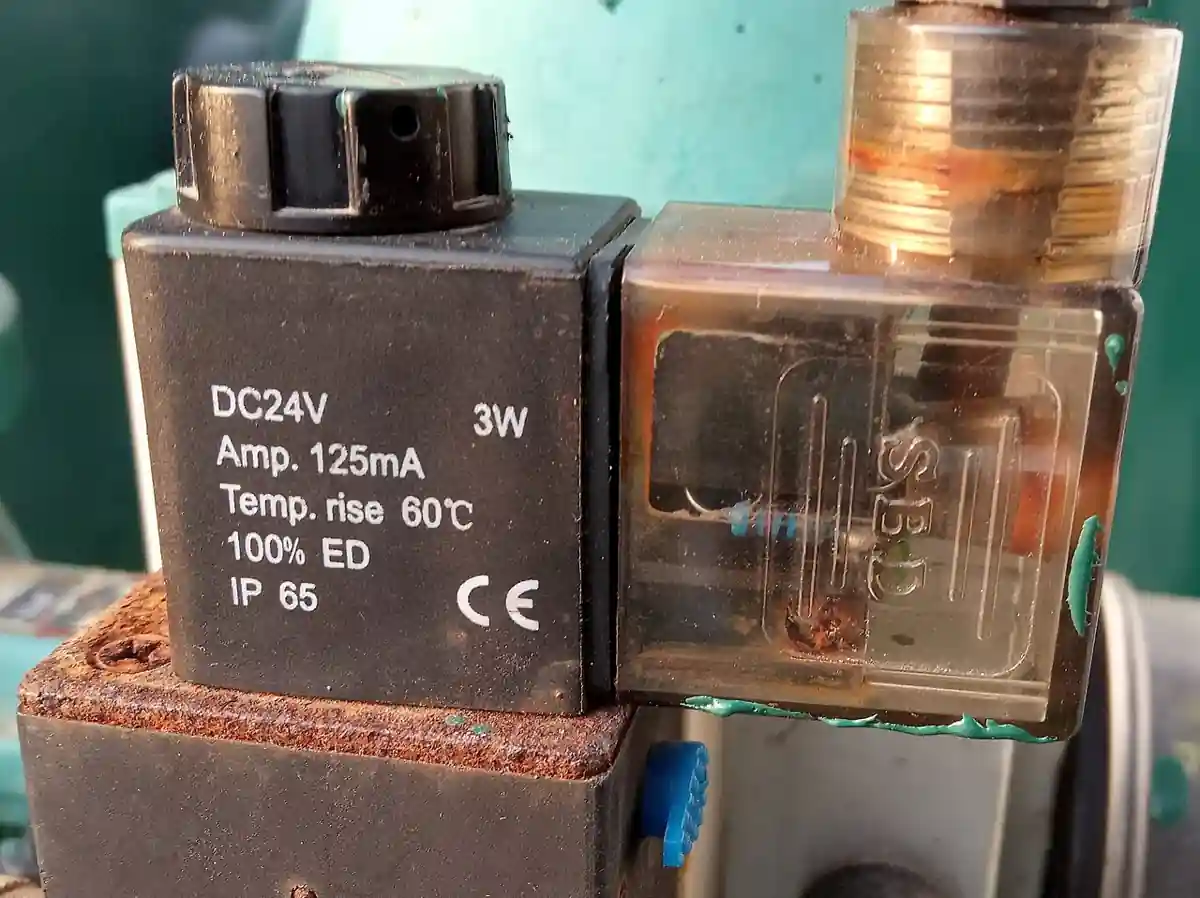 Encapsulated 24V DC solenoid coil on a pneumatic valve, marked DC24V 3W 100% ED IP65 CE, fitted with a DIN 43650 connector plug