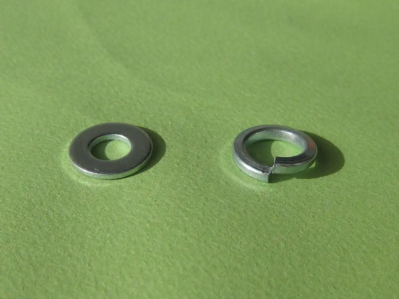 A plain flat washer beside a split helical spring lock washer, the steel coil ring with offset split ends that is the DIN 127 type of spring washer