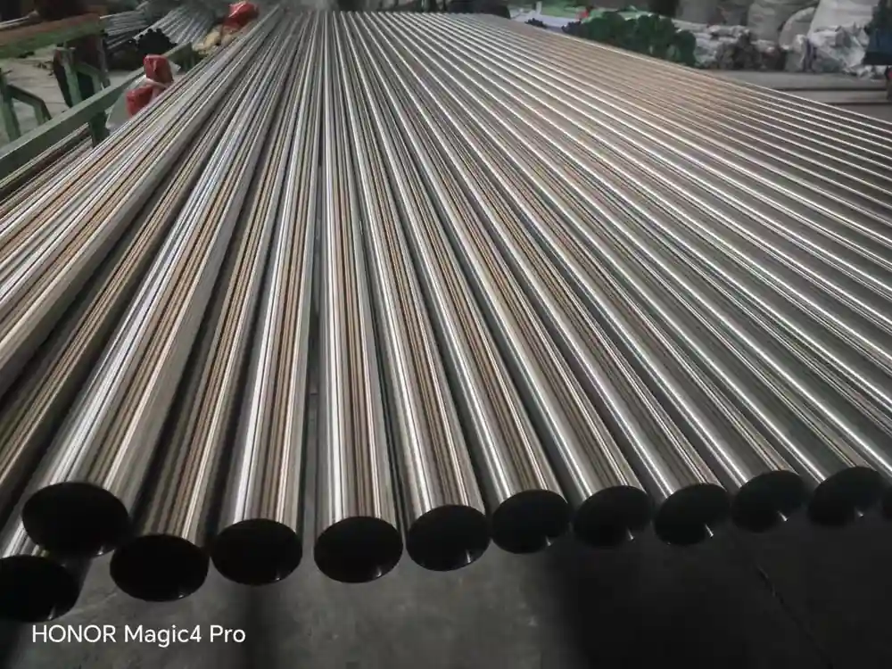 Rows of polished stainless steel pipes laid side by side with open ends toward the camera in a pipe mill warehouse