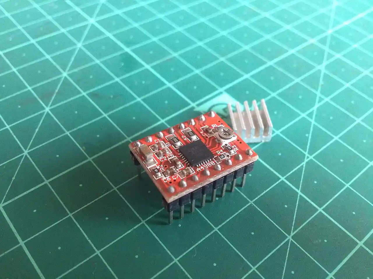 A4988 board-level stepper motor driver: a small red carrier PCB with the A4988 chopper driver chip, current-set trim potentiometer, header pins, and a clip-on heatsink, on a cutting mat