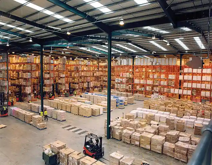 Multi-level steel pallet storage racks loaded with palletized cartons in a modern warehouse, with a forklift handling unit loads in the aisle