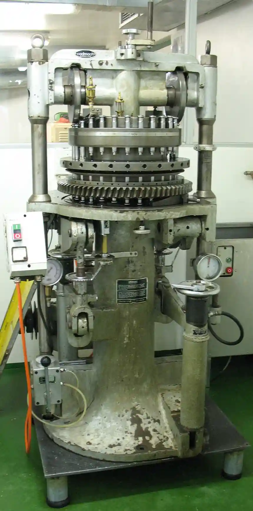 Cadmach-brand rotary tablet press, an industrial pharmaceutical tableting machine with a multi-station punch turret and compression rollers mounted on a pedestal