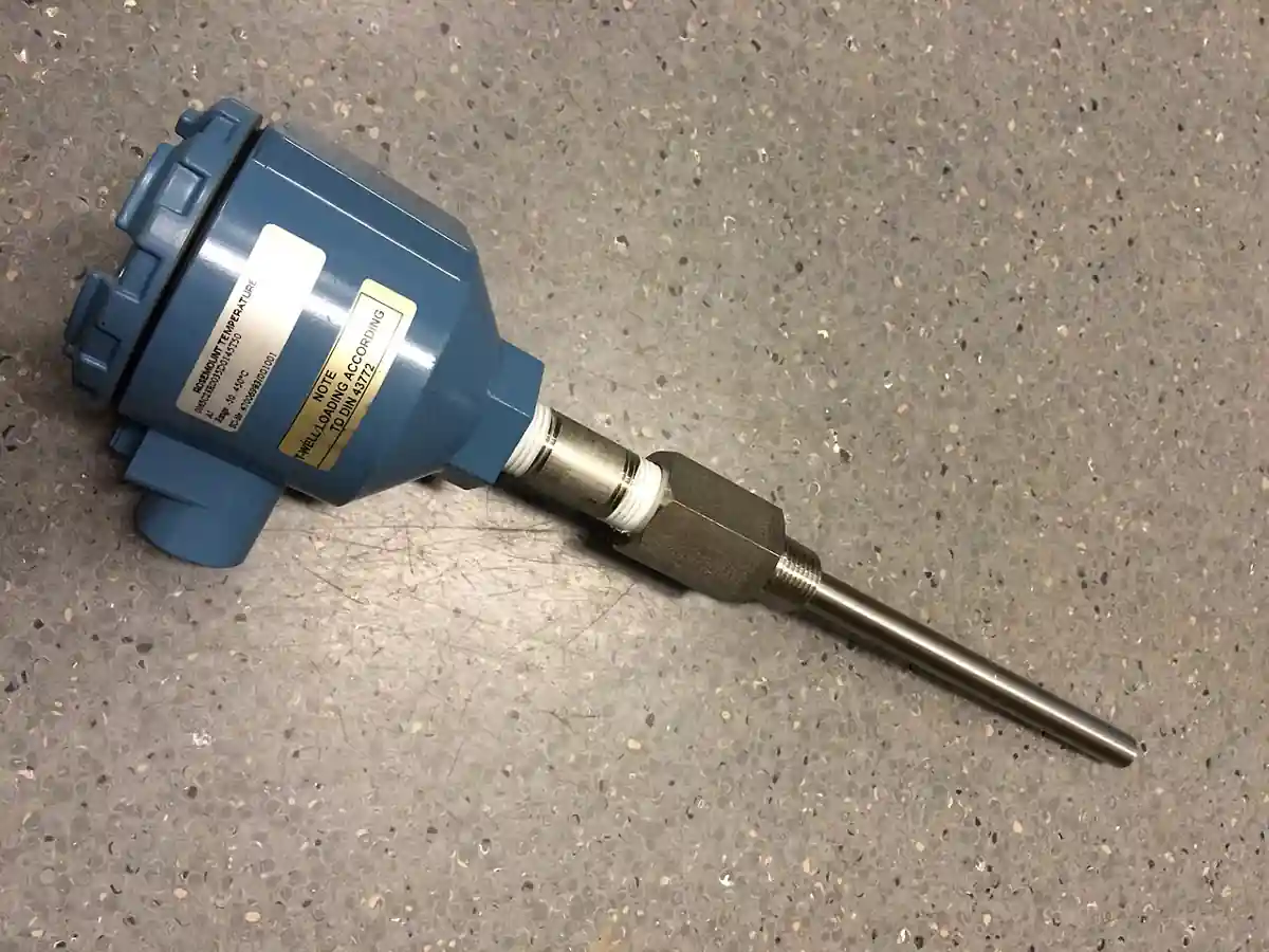 A blue Rosemount field-mount temperature transmitter housing connected by a hex nipple to a stainless-steel thermowell with an RTD/thermocouple probe, per DIN 43772