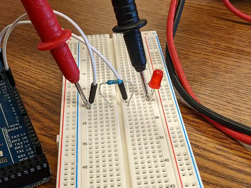 A red and a black multimeter test lead with insulated wires and sharp probe tips pressed into a breadboard to measure a resistor