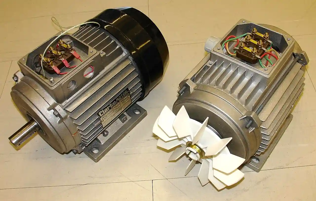 Two three-phase asynchronous (induction) motors with finned aluminium frames, foot mounting, shaft and exposed cooling fan, terminal boxes showing the six-stud three-phase connection block